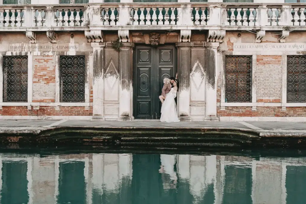 Ein Brautpaar in einer romantischen Szene mit Spiegelung im ruhigen Wasser des Kanals in Venedig – Hochzeitsfotograf Venedig.