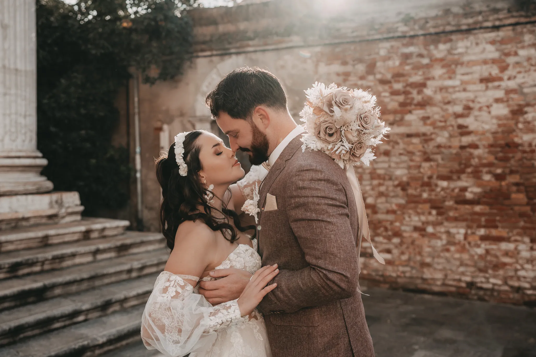 Inniger Kuss des Brautpaares vor einer Backsteinmauer mit Sonnenlicht – magische Momente beim Heiraten in Venedig.