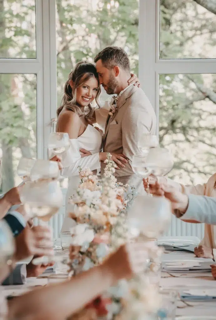 Brautpaar stößt mit Gästen beim Hochzeitsessen an