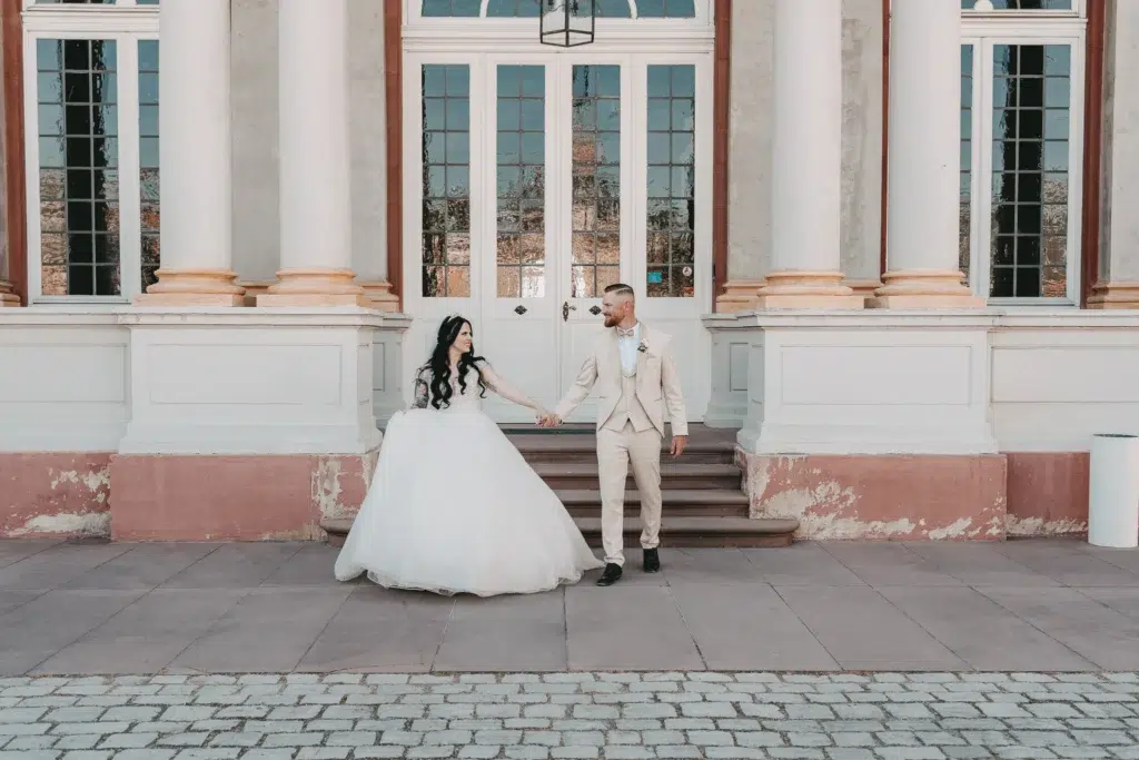 Hochzeitsreportage Karlsruhe – Brautpaar hält Hände vor prächtigem Barockschloss